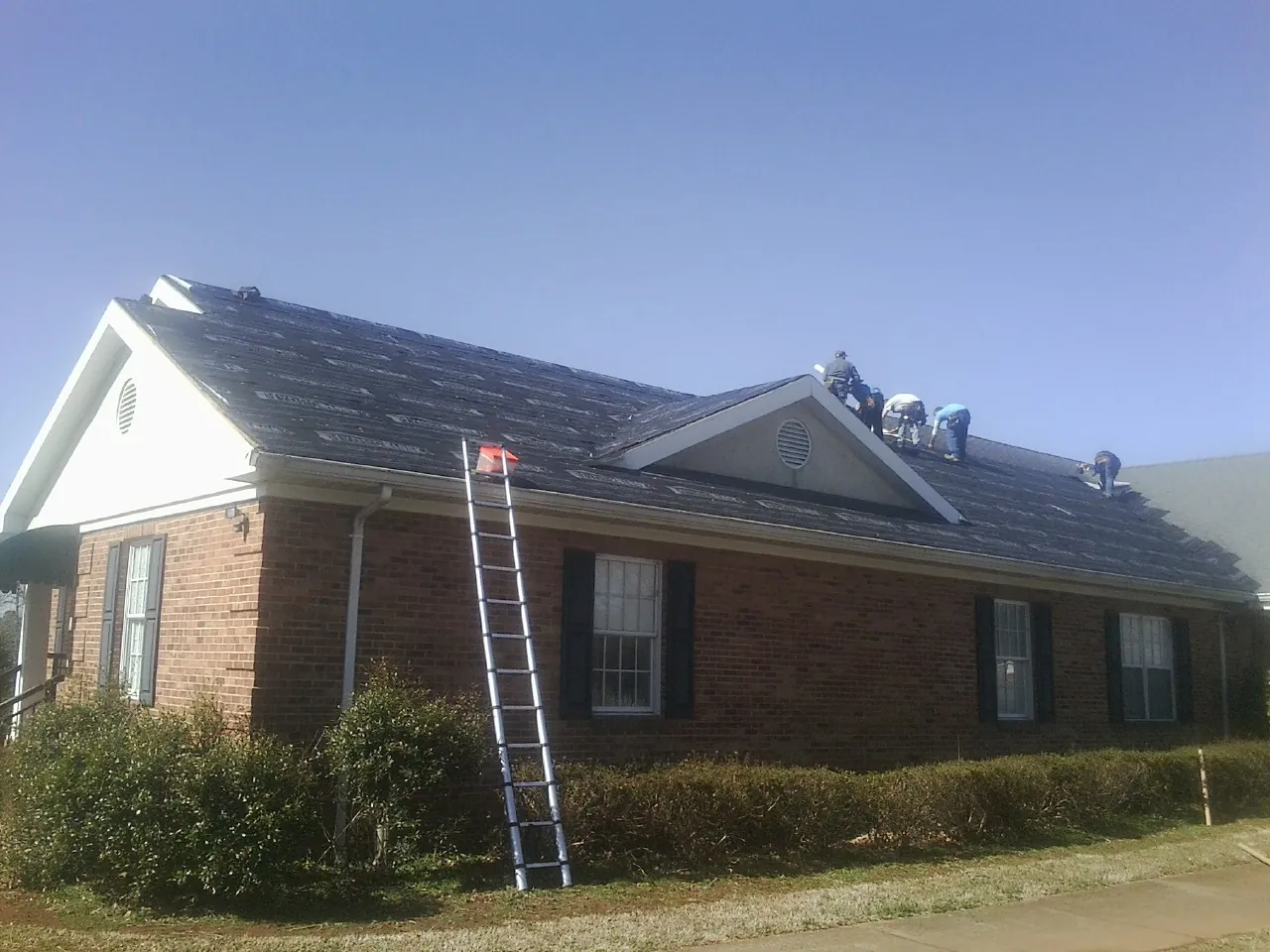 Crew tearing shingles off a brick ranch roof with a ladder set — Metal Roof Repair work by our crew in Paton