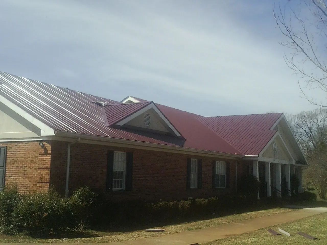 Red metal roof with gabled entries on a long brick building, from a Hail Damage Roof Repair job in Paton