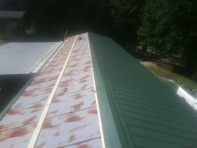 Old rusted panels beside newly installed green metal roofing — Wind Damage Roof Repair by Roofing Brothers in Paton