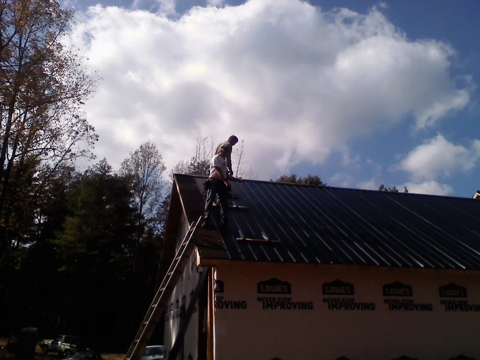 Roofer fastening dark metal panels high against a cloudy sky, from a Roof Inspection job in Paton
