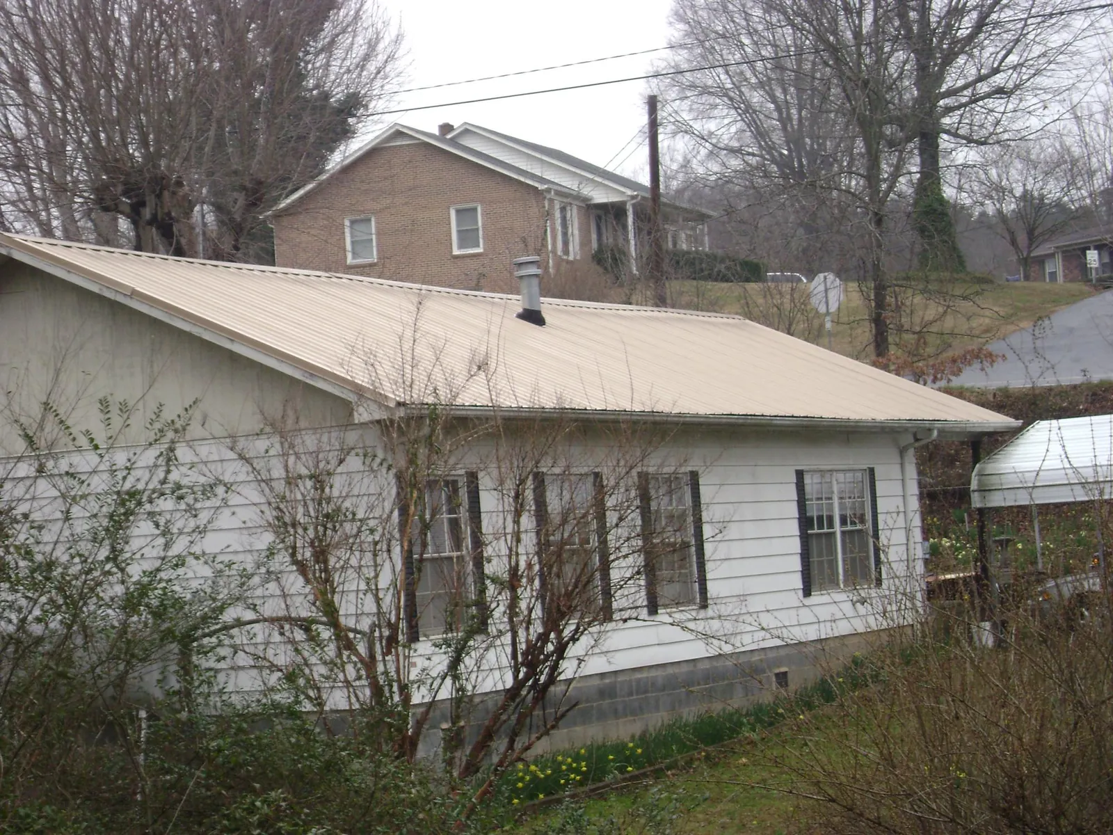 Tan metal roof on a white sided house set into a hillside — Commercial Roofing by Roofing Brothers in Paton