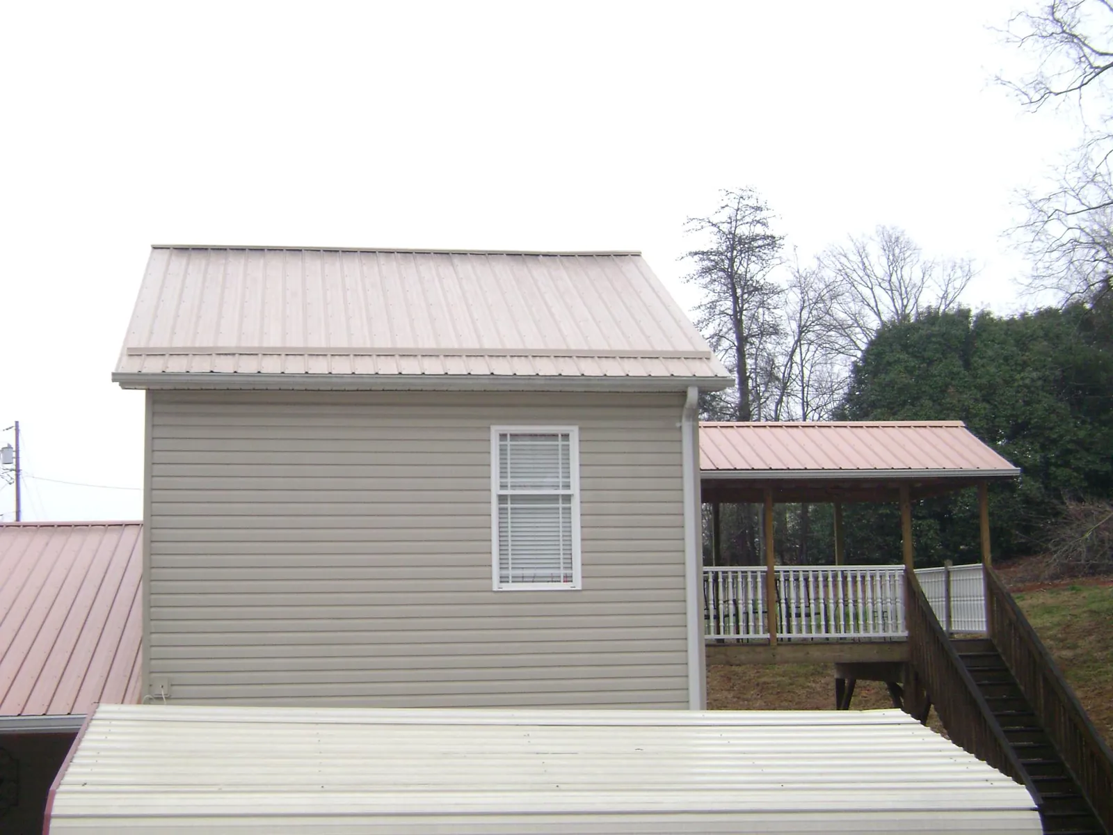 Tan metal roofs on a two story addition and attached porch, from a Roof Replacement job in Paton